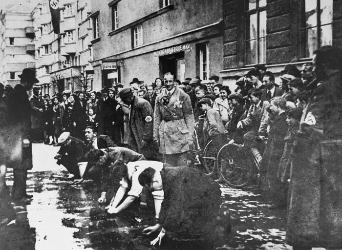 In this image, as part of a ritual of public humiliation, Jewish men and women were forced to scrub the streets to remove political slogans that were critical of Germany’s annexation of Austria.