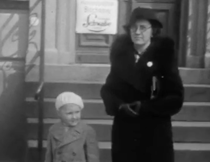 A woman and child walk in Berlin and interact with Nazi propaganda.